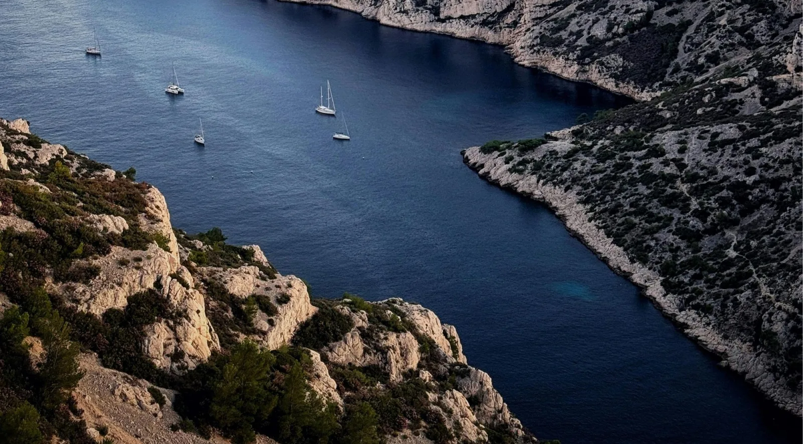 Dramatic aerial view of a deep narrow Calanques inlet with three sailboats far below