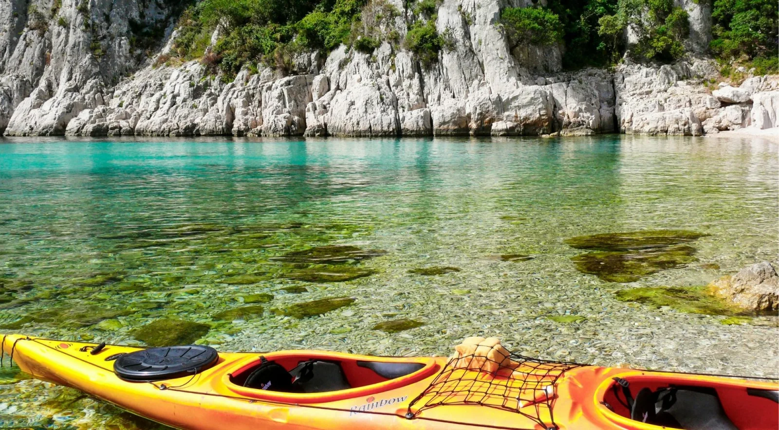 Sea kayaks on crystal-clear turquoise water beside white limestone rocks