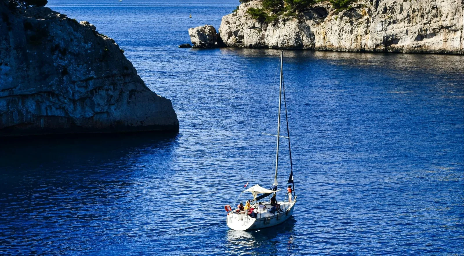Sailboat with guests sailing past limestone sea stacks in deep blue Calanques water