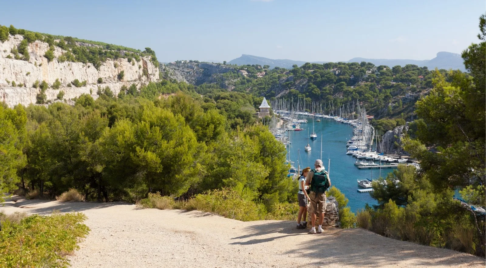 Two hikers looking down at Calanque de Port-Miou marina lined with sailboats below