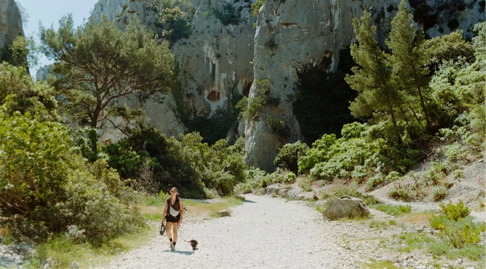 Woman hiking a rocky trail through garrigue scrubland beneath towering Calanques limestone cliffs